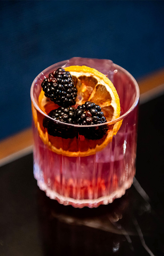 Blackberry cocktail in a rocks glass against a dark blue background