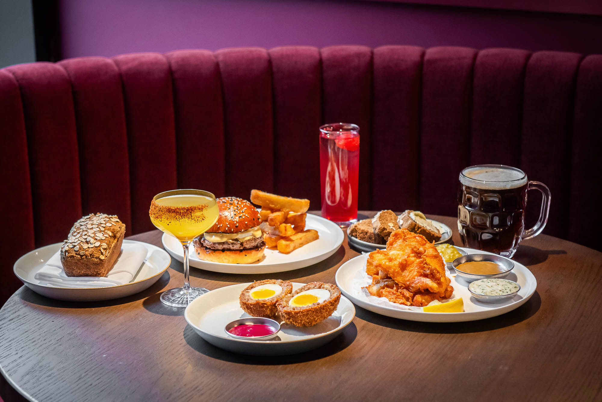 Bar bites and cocktails on a dark wood table against a red booth