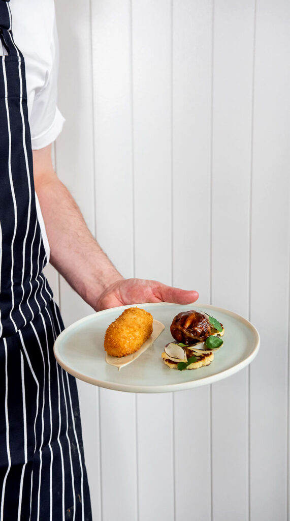 Chef wearing an apron holding Hen Kiev against a white wall